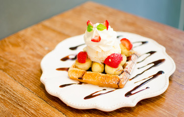 waffle with ice cream topping with strawberry and banana on wood