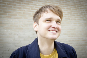 Handsome young man against brick wall smiling. Candid.