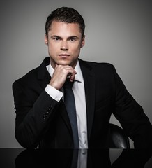 Handsome young well-dressed man in jacket  behind table