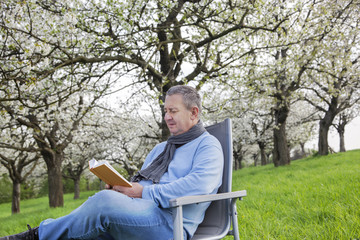 Man reading in the book under blooming cherry tree