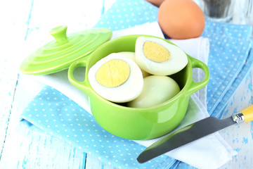 Boiled eggs in pan and eggcup on color wooden background