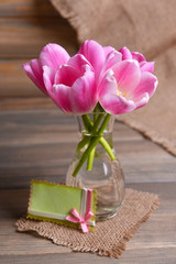 Beautiful tulips in bucket in vase on table on grey background