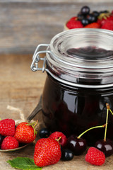 Tasty jam with berries in glass jar on wooden table
