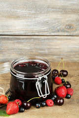 Tasty jam with berries in glass jar on wooden table