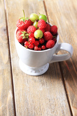 Forest berries in cup, on wooden table background