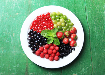 Forest berries on plate, on color wooden background