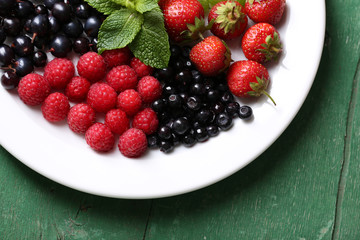 Forest berries on plate, on color wooden background
