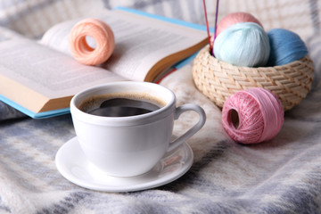Fototapeta na wymiar Cup of coffee and yarn for knitting on plaid with book