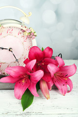 Beautiful lily with clock on wooden tray on bright background