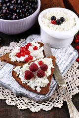 Bread with cottage cheese and berries on wooden board close-up