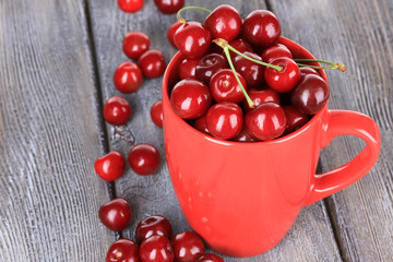 Sweet cherries in mug on wooden background