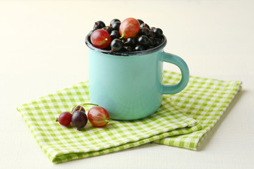 Ripe blackcurrants in mug on light wooden background.