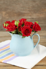 Bouquet of red roses in vase on wooden background