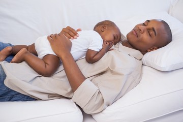 Happy father napping with baby son on couch