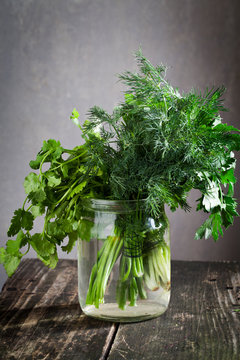 dill with parsley and coriander in a jar on a wooden board