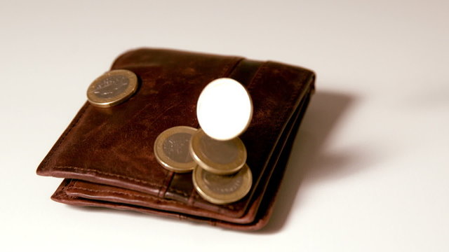 Euro coins falling over brown leather wallet on white surface
