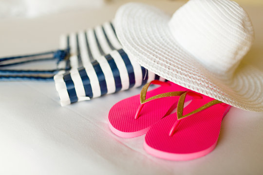close-up of beach bag, hat and flip-flops on bed