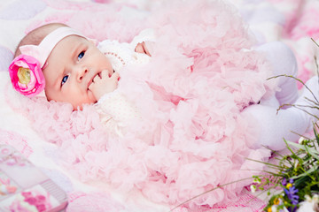 Fototapeta na wymiar cute newborn girl in pink skirt gnaws fingers
