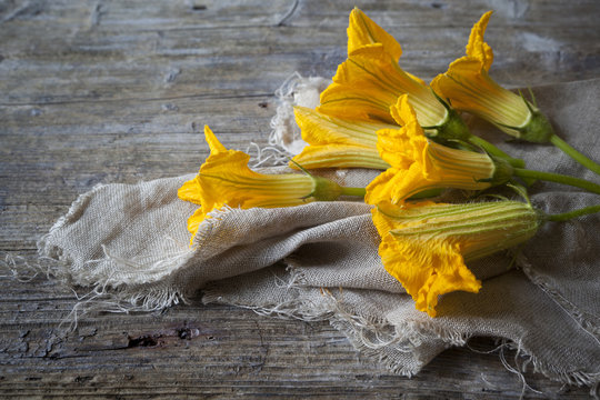zucchini blossoms lying on rustic wooden table with jute napkin