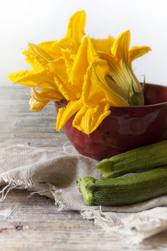 whole zucchini and zucchini blossoms on red bowl on rustic table