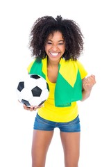 Pretty football fan holding brazilian flag cheering at camera