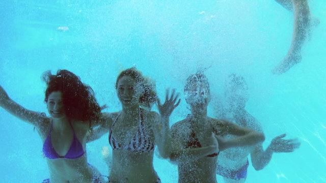 Four friends jumping into swimming pool and waving