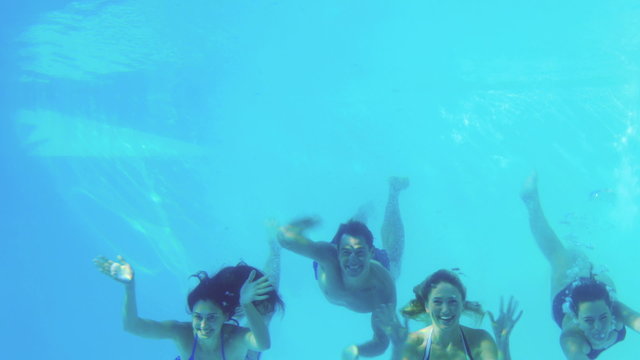 Four friends jumping into swimming pool and waving
