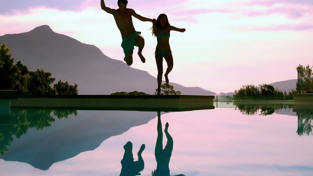 Couple jumping into swimming pool holding hands