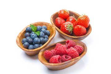 raspberries, blueberries and strawberries in a wooden bowls