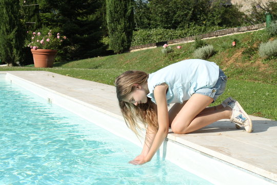 Bambina gioca con le mani dell'acqua dal bordo della piscina