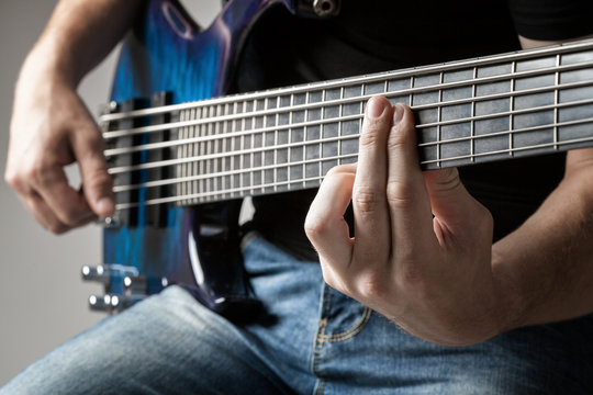 male musician playing on six-string bass guitar