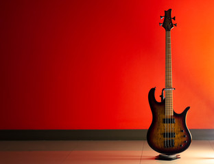 Single bass guitar against red wall - obrazy, fototapety, plakaty
