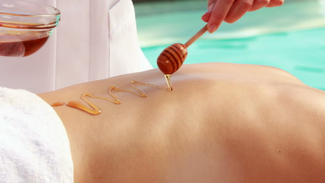 Beauty therapist pouring honey onto womans back
