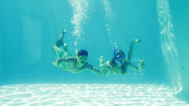 Happy couple jumping into swimming pool wearing snorkels and hol