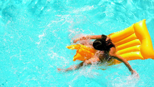 Brunette splashing on lilo in the swimming pool