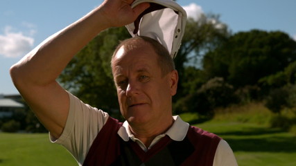 Mature golfer taking off his cap on a hot day