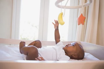 Fototapeten Adorable afro-american baby boy lying in his crib playing with mobile © WavebreakMediaMicro