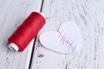 Broken heart and thread on wooden background