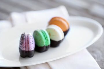 Colorful macaroons in plate on wooden table, close-up