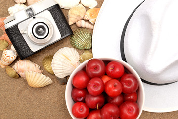 Red plums, old camera, shells and white hat on sand