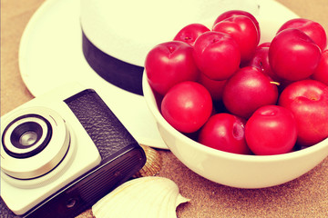 Red plums, old camera, shells and white hat on sand