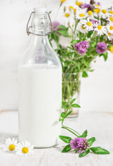 Obraz na płótnie Canvas Fresh milk in old fashioned bottle and wildflowers