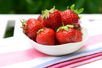 Ripe sweet strawberries in bowl on table in garden