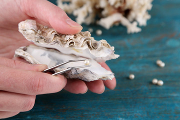 Hand with tweezers holding pearl and oyster on wooden
