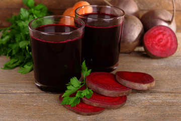 Glasses of fresh beet juice and vegetables on wooden background