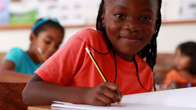 Little girl writing and smiling at camera during class