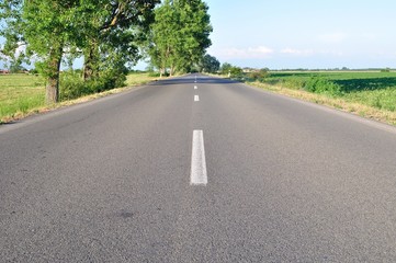Obraz premium Asphalt road with green trees and blue sky