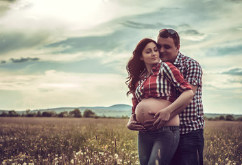 husband and his pregnant wife are walking at sunset in field on
