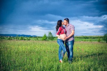 husband and his pregnant wife are walking at sunset in field on