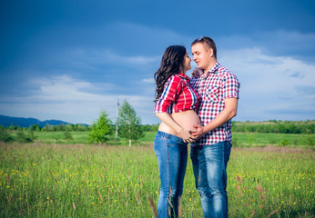 husband and his pregnant wife are walking at sunset in field on